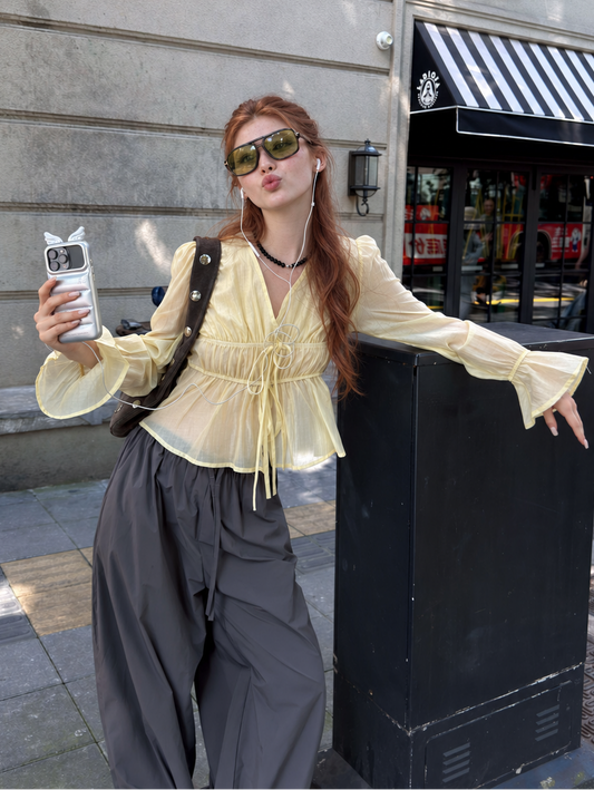 Woman wearing the Butter Veil Ethereal Drawstring Sheer Blouse with relaxed wide-leg trousers on a city street.