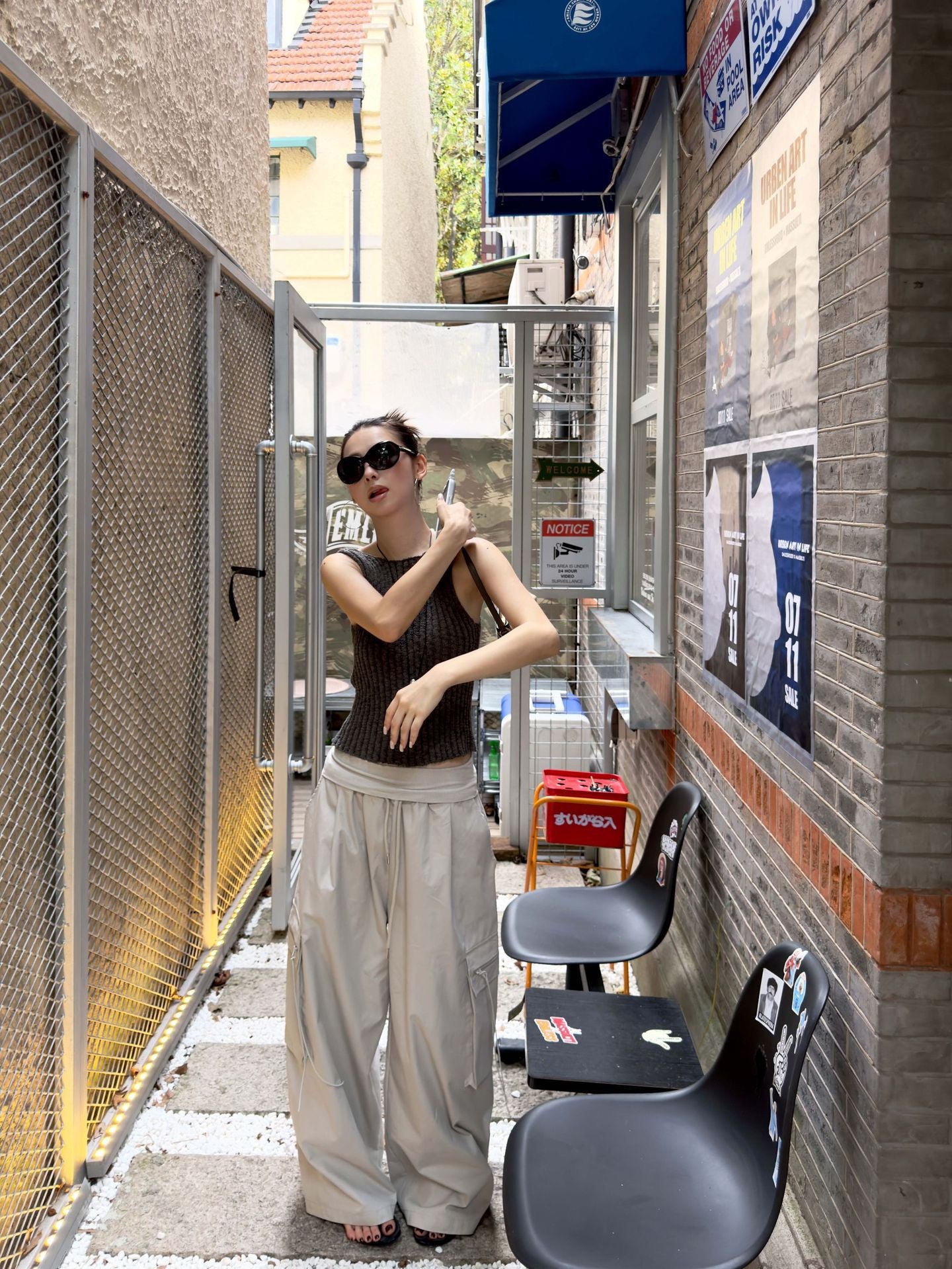 Model wearing Vintage Foldover Waist Wide Leg Cargo Pants in Stone Mist with a dark ribbed knit tank in an urban alley setting.