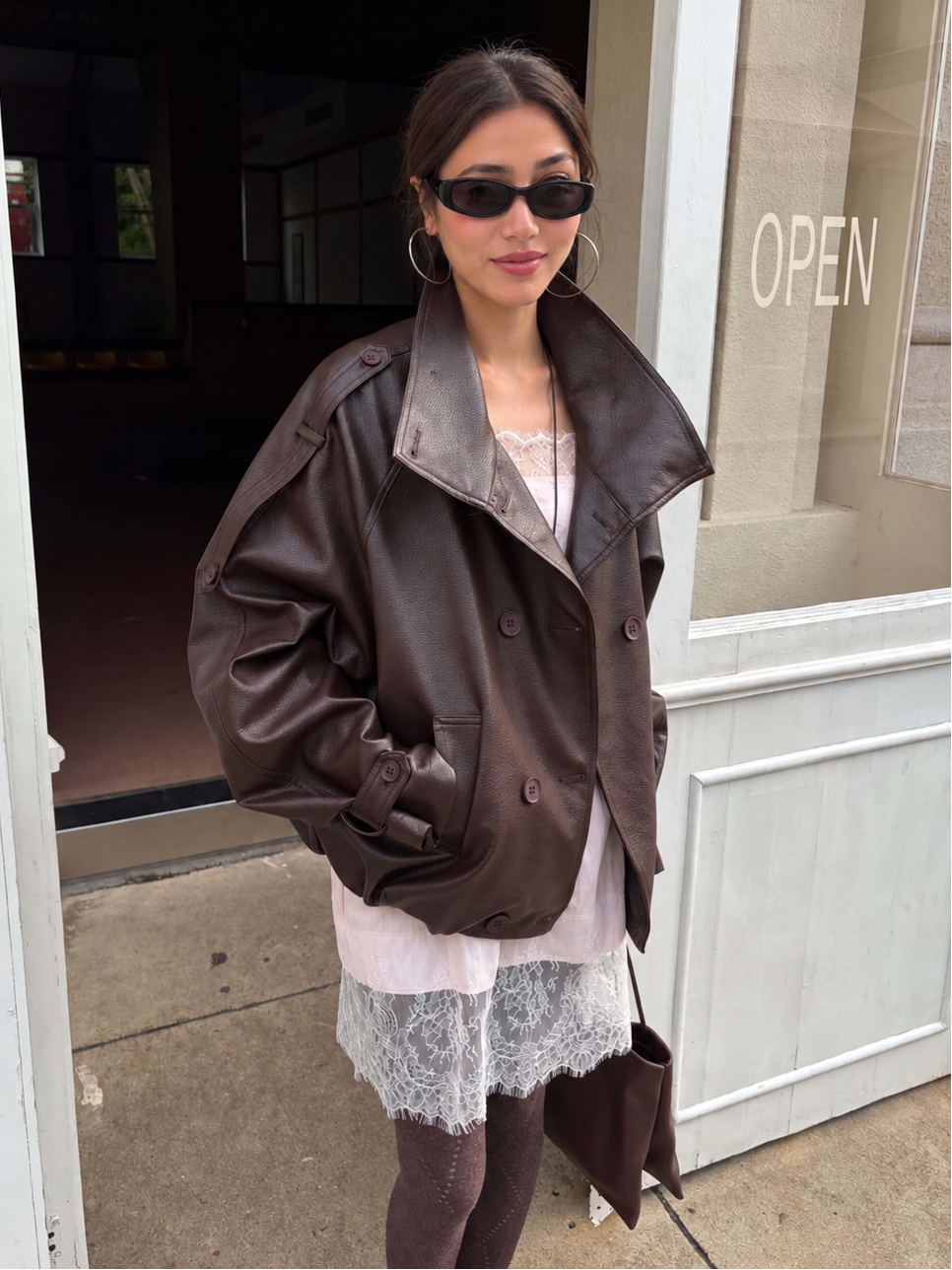 Front view of the Avery Oversized Faux Leather Moto Jacket in Espresso Brown styled with a lace mini dress and sheer tights.